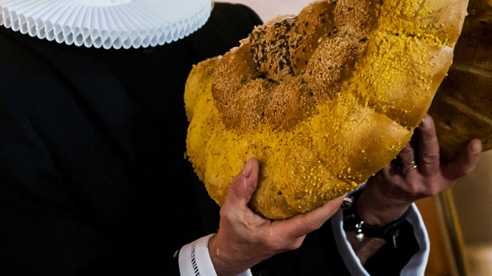 En person holder et stort, gyldenbrunt brød eller wienerbrød med en smuldrende topping.