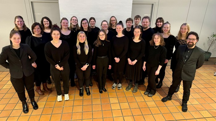 Gruppe af mennesker i formelt sort tøj, der poserer sammen indendørs til et gruppefoto.