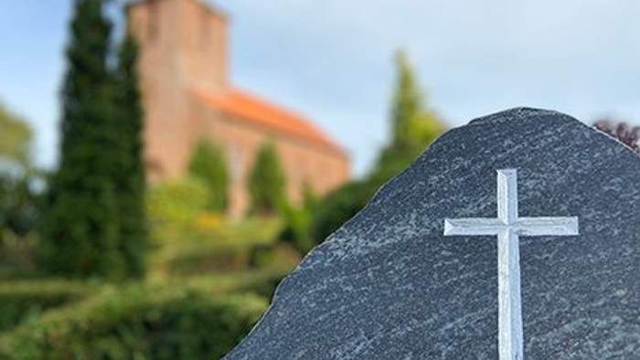 En gravsten med kors foran kirke.