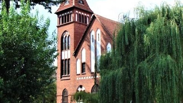 Ein rotes Backsteingebäude mit spitzem Turm und grünem Garten