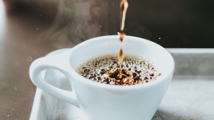 Kaffee wird in eine weiße Tasse auf einem Tablett gegossen