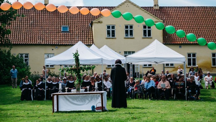 En præst holder tale under et åbenluftsevent med mange tilstedeværende.