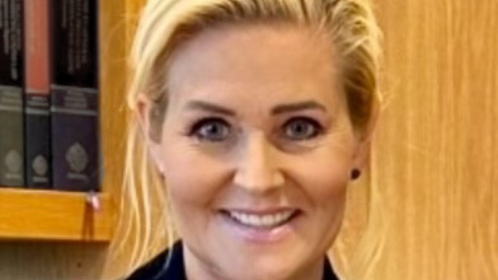Professionel kvinde med blondt hår, der smiler foran en bogreol med juridiske bøger.