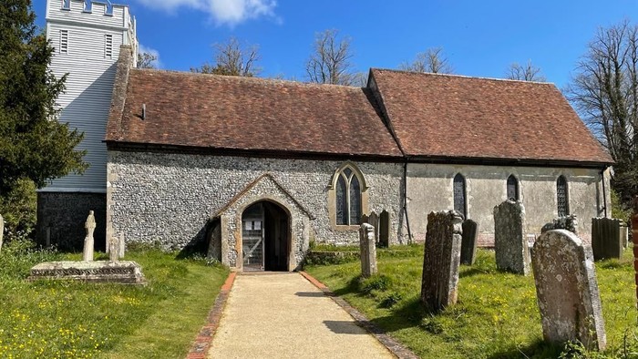 Quaint stone church with arched entrance, gravestones, and a tall bell tower under a clear sky.