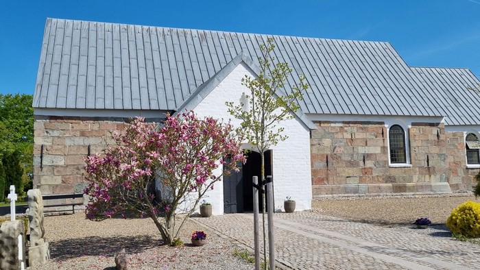 Et moderne hus med metaltag og stenfacade, omgivet af træer og blomster.