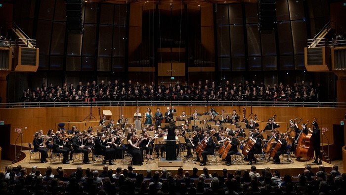 Ein großes Orchester spielt in einem prächtigen Konzertsaal vor vollem Publikum