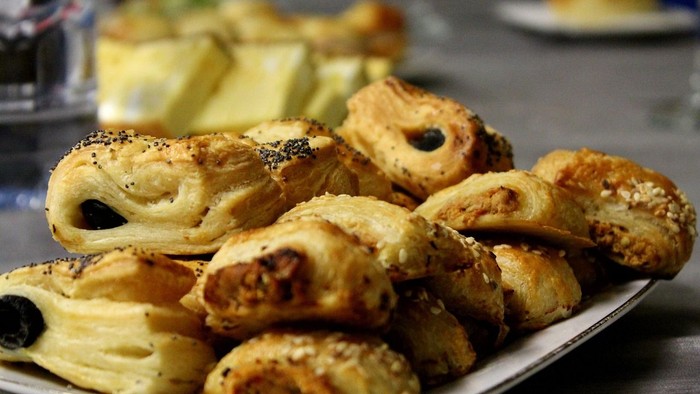 Golden, sesame-topped pastries arranged neatly on a white plate, likely a type of baklava or similar treat.