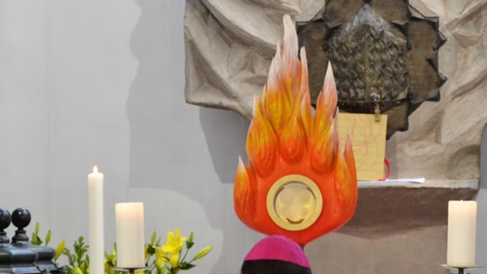 Ein Priester führt eine Messe in einer Kirche durch, vor einem Altar mit Flammen und Kerzen.