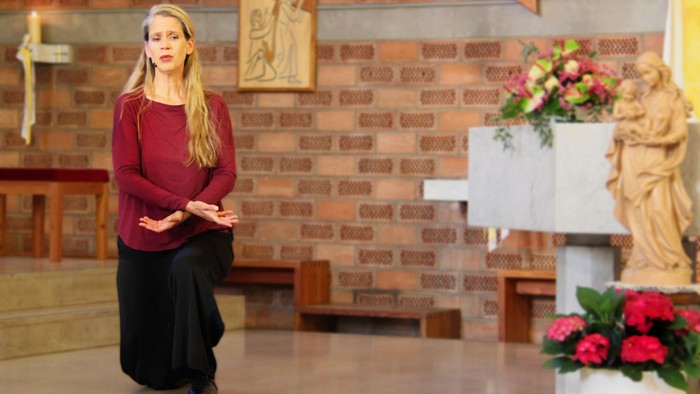 Eine Frau in einem bordeauxroten Oberteil spricht in ein Mikrofon in einer dekorierten Kircheninnenraum mit Blumenarrangements.