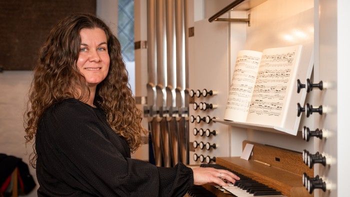 En kvinde spiller på et orgel med noderne åbne foran sig og smiler varmt.