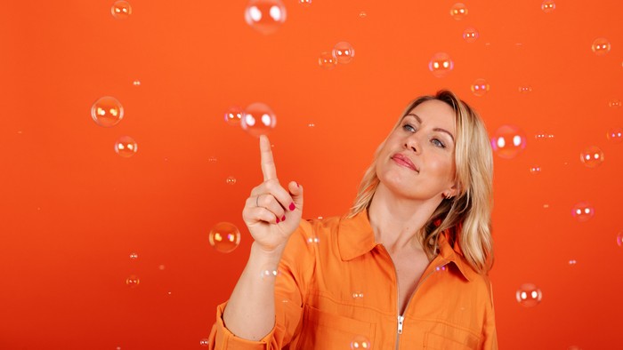En person i en orange trøje laver bobler med fingeren mod en klar rød baggrund.