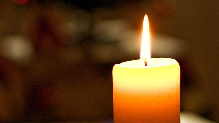 Kerze im Halter mit brennendem Docht, bunte Lichter im Hintergrund