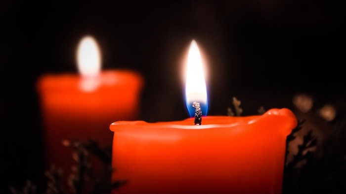 Zwei brennende Kerzen, eine im Fokus, eine unscharf im Hintergrund.