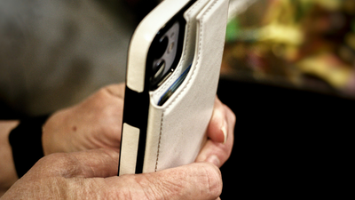 Eine Person hält ein Smartphone mit einer weißen Schutzhülle und macht ein Foto im Freien.