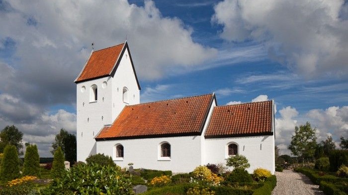 Et hvidt kirkebygning med røde tag og en have med blomster.