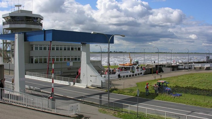 Ein geschäftiger Fährterminal mit Menschen, die an einer Uferpromenade Schiffe besteigen, unter einem teilweise bewölkten Himmel.