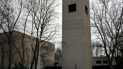 Hohes Ziegelgebäude mit kleinen Fenstern, umgeben von kahlen Bäumen.