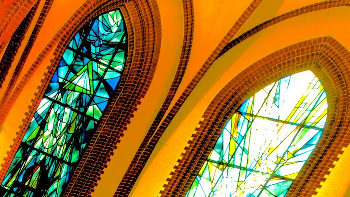 Buntglasfenster in einer Kathedrale erzeugen durch bogenförmige Designs lebendige, farbenfrohe Lichtmuster.