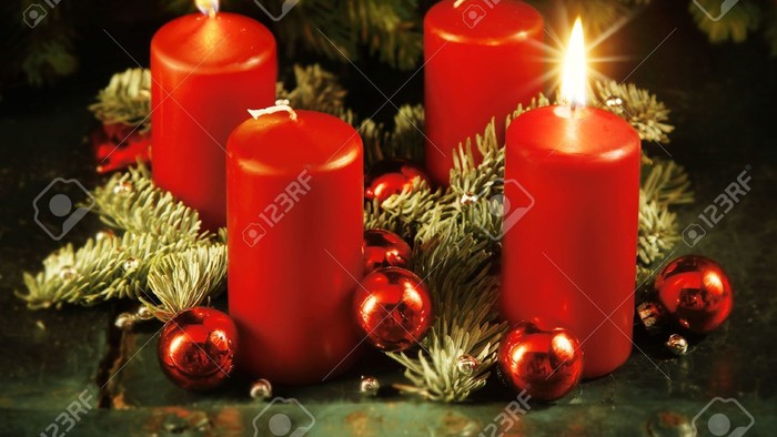 Vier rote Kerzen, umgeben von Tannenzweigen und festlichen roten Christbaumkugeln auf einer rustikalen Holzoberfläche.