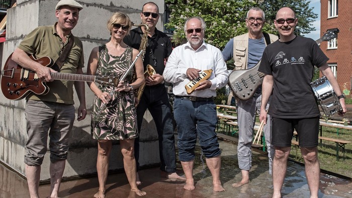 Sechs Musiker von Soundpool stehen mit ihren Instrumenten in den Händen und naccktn Füßsen in einer Pfütze