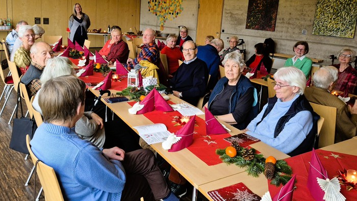 Gruppe älterer Menschen, die sich an einem festlich gedeckten Tisch mit dekorierten Tischsets und festlichem Grün versammelt haben.