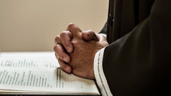 En person med sammenflettede hænder sidder foran en åben bog.