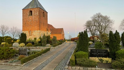 En gammel kirke med tårn og røde tag, omgivet af en park med buske og steder.