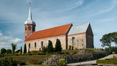 En gammel kirke med spiret og røde tagtaver på en bakketop under et blødt himmel.