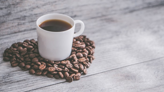 En lille hvid tekt med kaffe og kaffebønner på et træbord