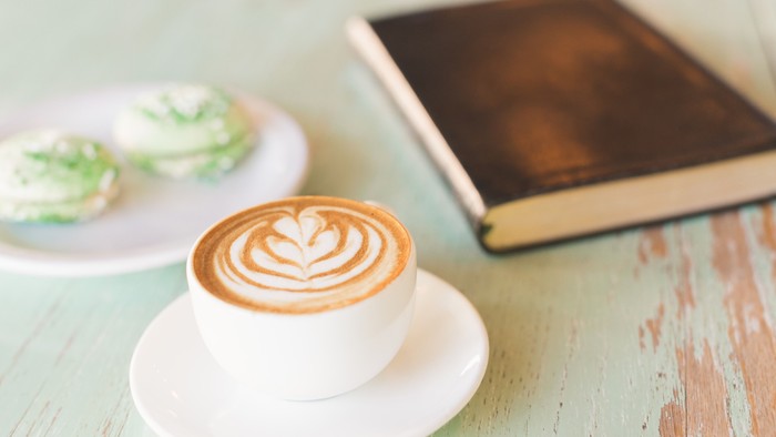 Ein Cappuccino, zwei Muffins und ein Buch auf einem grünen Tisch