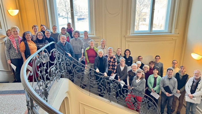 Eine vielfältige Gruppe posiert gemeinsam auf einer prächtigen Treppe in einem eleganten Innenraum.