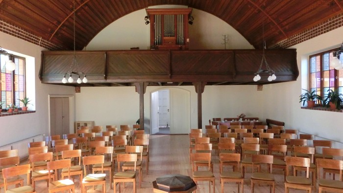 Großer leerer Saal mit Holzstühlen und hohem gewölbtem Deckengewölbe.