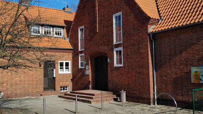 Rotes Backsteingebäude mit steilem Dach und Solaranlagen unter klarem, blauem Himmel.