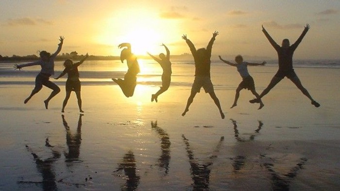 Fem børn springer på stranden ved solnedgang