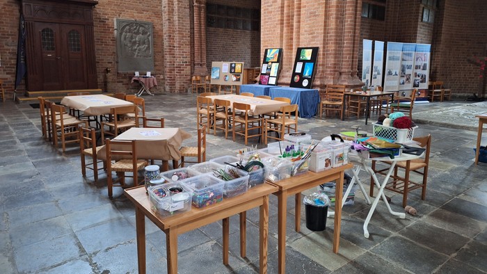 Kunstmaterialer lagt frem på borde i et stort rum med murstensvægger og buer.