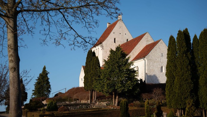 Hvid bygning med rødt tag omgivet af træer.