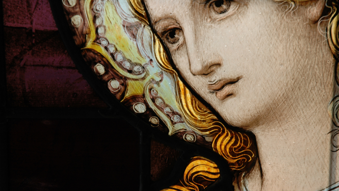 Indviklet glasmosaikportræt af en rolig, gloriefyldt kvindelig figur med prægtigt hovedsmykke.