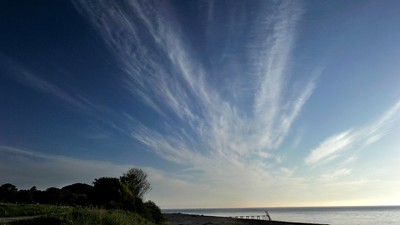 Fredfyldt kystlinje med sarte skyer, der danner slående mønstre mod en klar blå himmel.