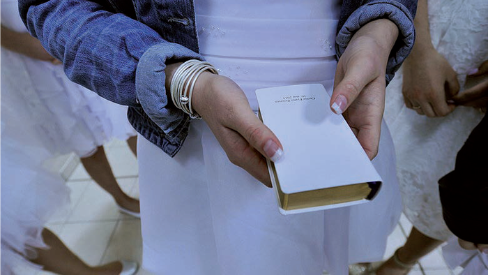 Person holder en åben bog under en religiøs ceremoni med andre i hvidt tøj.