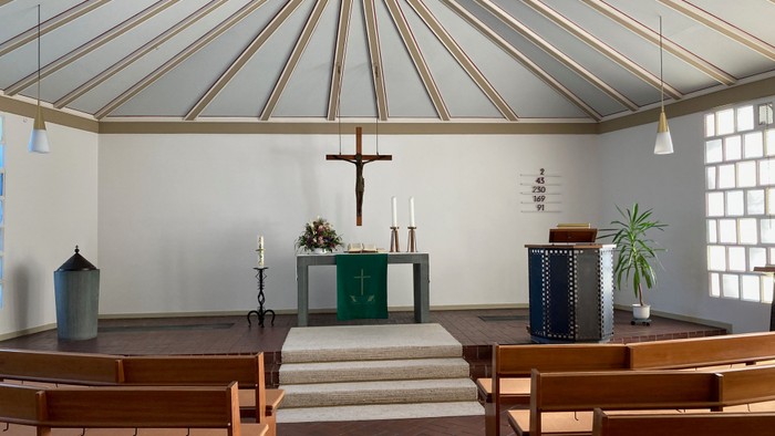 Kleine, helle Kirche mit Holzstühlen, Kreuz und Altarraum