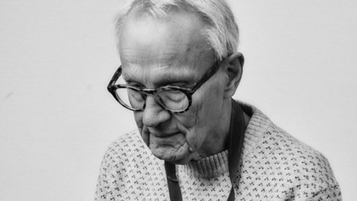 En ældre mand med briller holder eftertænksomt et gammeldags kamera.