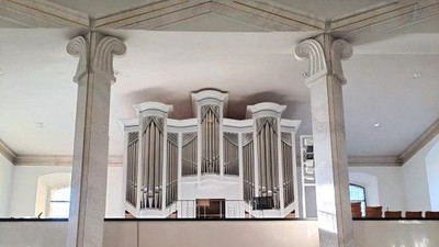 Elegante Kircheninnenausstattung mit einer großen Pfeifenorgel, die auf klassischen Säulen erhöht steht, sowie gestuften Sitzreihen und Kirchenbänken.