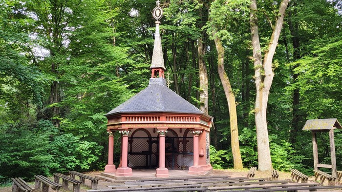 Idyllischer hölzerner Pavillon mit Spitze, eingebettet in eine üppige, grüne Waldlandschaft.