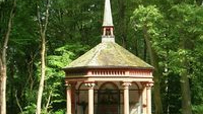 Idyllischer Pavillon mit Uhrturm, eingebettet zwischen üppigen Waldbäumen, umgeben von Holzbänken.