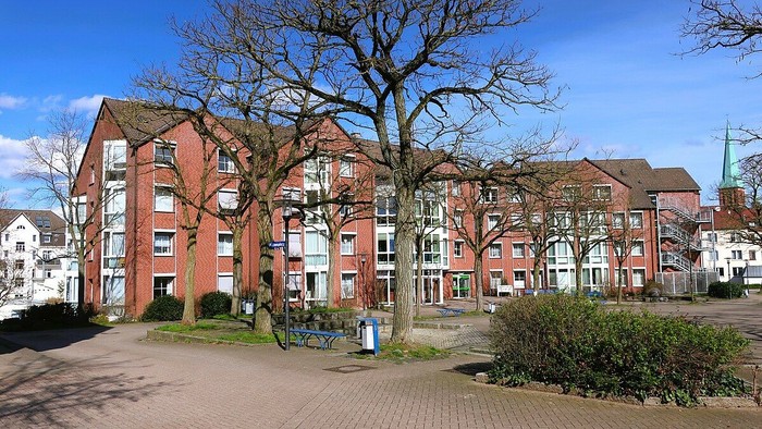 Ein Wohnkomplex mit roten Backsteingebäuden und einem großen Baum im Vordergrund.