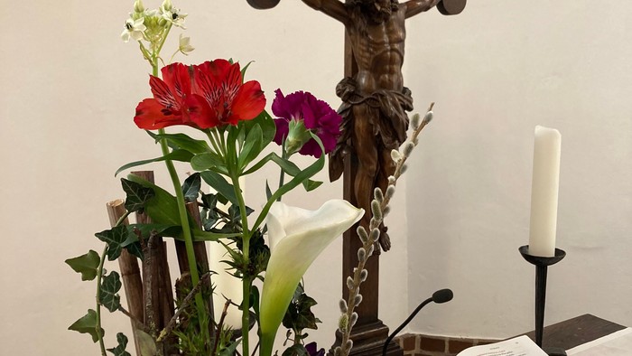 Ein Kreuz mit Jesusfigur, ein Blumenstrauß und eine aufgeschlagene Bibel