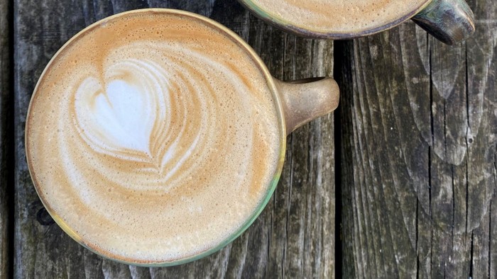 Ein Latte mit einem herzförmigen Milchschaumdesign steht in einer Keramiktasse auf einer rustikalen Holzoberfläche.