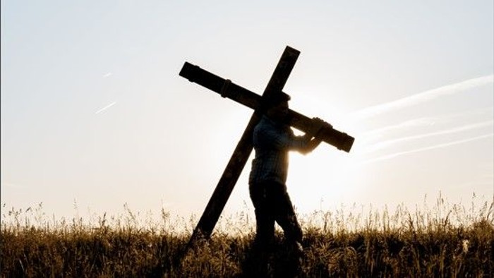 Person trägt Kreuz durch Feld bei Sonnenuntergang