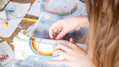 En person maler omhyggeligt et regnbue-design på en lille dekoration med finpudsede tuscher.