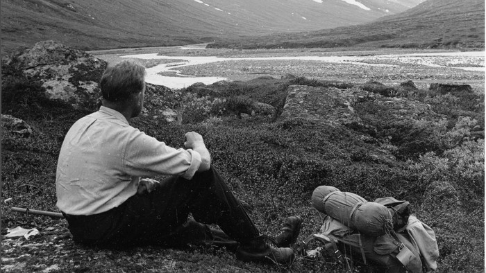 To vandrere hviler og slapper af i et fredfyldt bjerglandskab med udsigt til en malerisk sø.